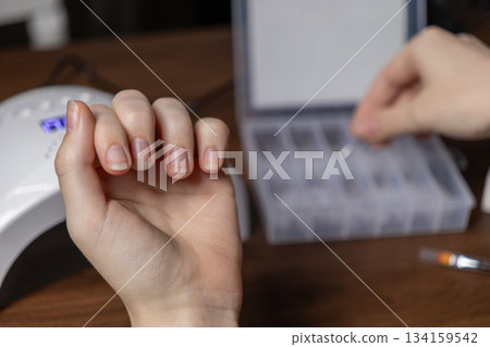 Woman's natural nails getting ready for a DIY manicure, with her other hand selecting nail extension upper forms from a kit, highlighting home beauty 134159542