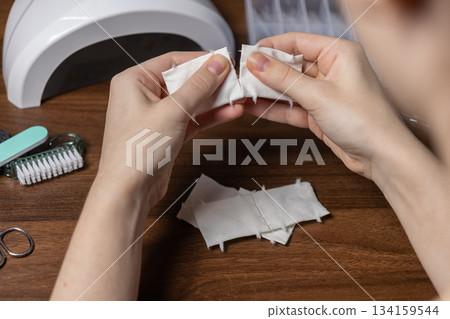 Female hands meticulously prepare small white cotton pads, tearing them for a professional DIY manicure, a focused personal beauty treatment 134159544