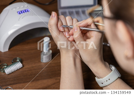 Person performs manicure by oneself at home, carefully pushing cuticles with a metal tool, demonstrating personal beauty care and self-grooming ritual Person performs manicure by oneself at home, carefully pushing cuticles with a metal tool, demonstrating personal beauty care and self-grooming ritual 134159549