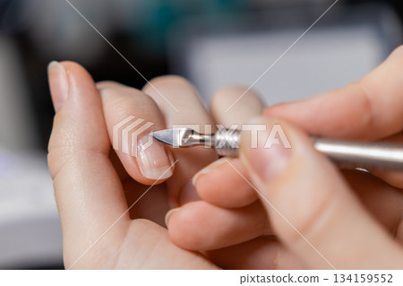 Woman's hand carefully pushing cuticles with a metal tool during a self-manicure, promoting personal beauty routine, self-care, and nail grooming at home 134159552