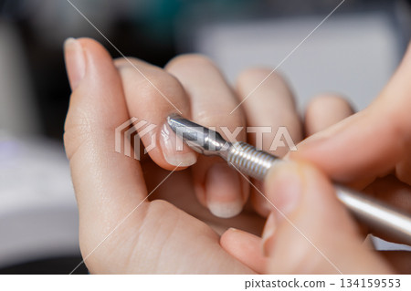 Woman performing self-manicure, meticulously pushing back cuticles on natural fingernails using a metal tool for essential personal nail care and beauty 134159553