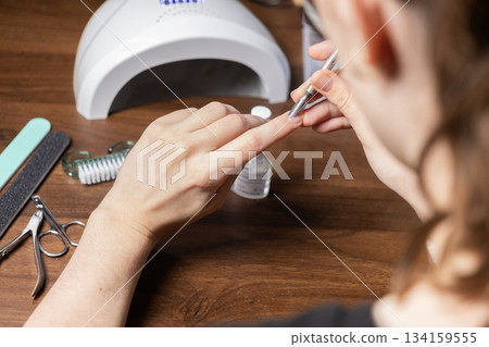 Young woman performing a meticulous DIY manicure by herself, carefully pushing back cuticles with a metal tool for personal beauty routine 134159555