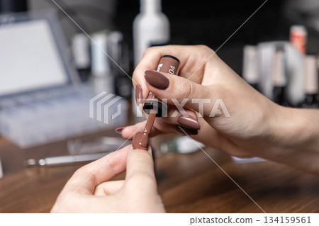 Close-up of a woman's hands meticulously applying brown nail polish to her fingernail, performing a professional self-manicure for personal grooming and beauty care Close-up of a woman's hands meticulously applying brown nail polish to her fingernail, performing a professional self-manicure for personal grooming and beauty care 134159561
