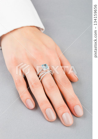 Beautiful female hand with gold ring with diamonds and aquamarine on gray background 134159656
