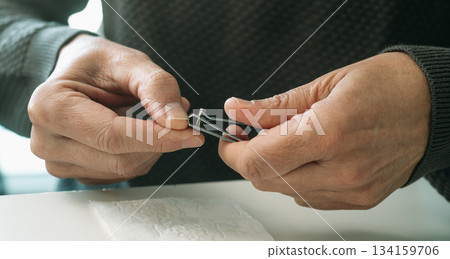 a man trims his thumb nail with precision a man trims his thumb nail with precision 134159706