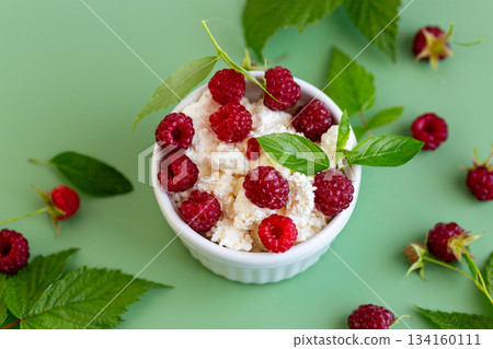 Cottage cheese with raspberries and green leaves on a green background 134160111