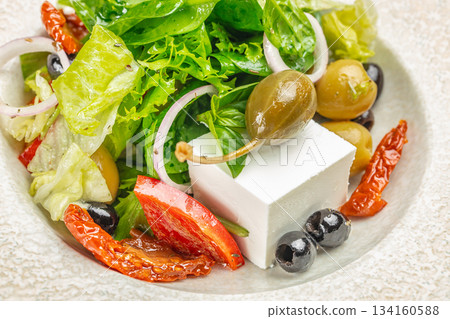 Fresh Greek salad with feta cheese, olives, caper berries, sun-dried tomatoes, and crisp greens close-up Fresh Greek salad with feta cheese, olives, caper berries, sun-dried tomatoes, and crisp greens close-up 134160588