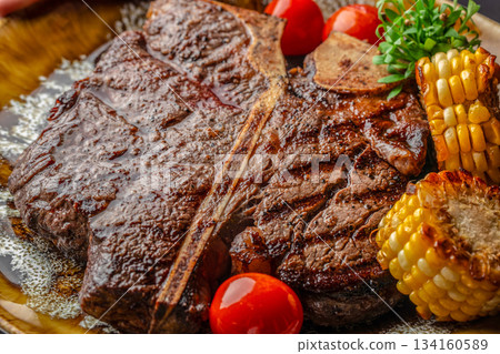 Juicy grilled T-bone steak with charred corn and cherry tomatoes served in a rich buttery sauce, restaurant menus, advertising and premium culinary branding Juicy grilled T-bone steak with charred corn and cherry tomatoes served in a rich buttery sauce, restaurant menus, advertising and premium culinary branding 134160589
