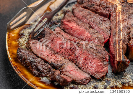 Juicy medium rare grilled T-bone steak sliced on plate with steak knives, close-up of tender beef meat with seasoning and juices 134160590