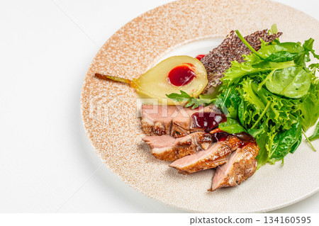 Gourmet sliced duck breast with red berry sauce, fresh green salad and poached pear elegantly served on a modern plate 134160595