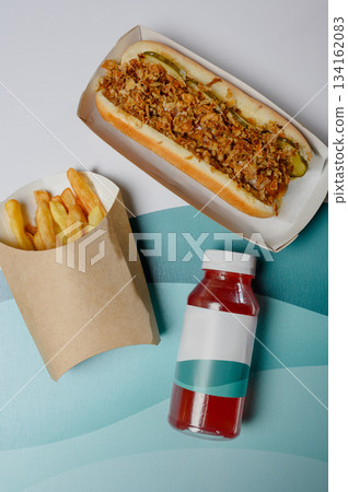 Hot dog with fried onions, french fries and ketchup in a bottle, top view. 134162083