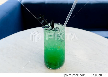 Bright green cocktail with ice and dark garnish in a glass on the table. Bright green cocktail with ice and dark garnish in a glass on the table. 134162095