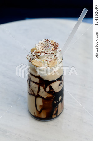 Iced coffee with chocolate syrup, whipped cream and peanuts on a white table 134162097