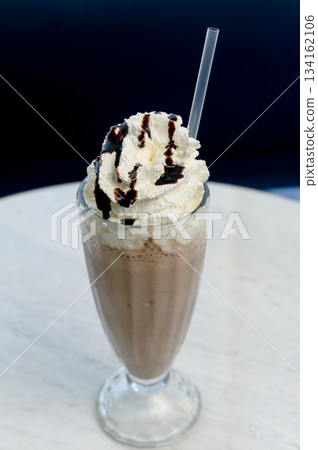 Chocolate milkshake with whipped cream and cocoa chips in a tall glass. 134162106