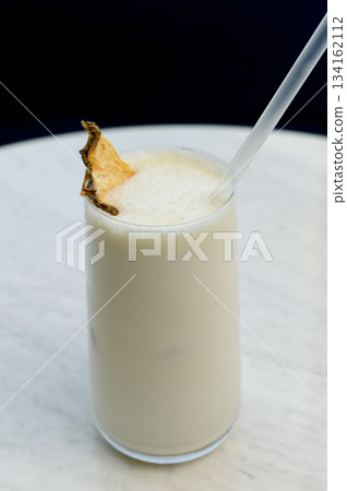 Vanilla milkshake with ice garnished with dried pineapple and a straw Vanilla milkshake with ice garnished with dried pineapple and a straw 134162112