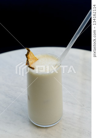 Vanilla milkshake with ice garnished with dried pineapple and a straw Vanilla milkshake with ice garnished with dried pineapple and a straw 134162114