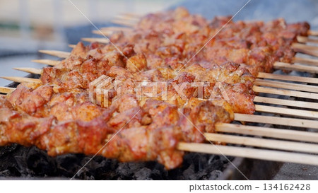 Juicy pork pieces on skewers, Tender and flavorful meat cooked over fire, Spiced meat skewers grilled to perfection at festive event, Delicious smoky pork bites served hot at lively outdoor food Juicy pork pieces on skewers, Tender and flavorful meat cooked over fire, Spiced meat skewers grilled to perfection at festive event, Delicious smoky pork bites served hot at lively outdoor food 134162428