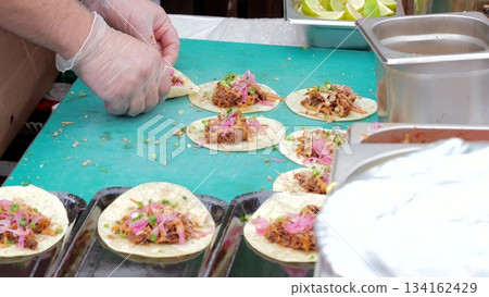 Market taco preparation, Vibrant street food assembly, Busy vendor crafting flavorful tacos quickly, Dynamic market scene with hands creating flavorful Mexican tacos using colorful ingredients Market taco preparation, Vibrant street food assembly, Busy vendor crafting flavorful tacos quickly, Dynamic market scene with hands creating flavorful Mexican tacos using colorful ingredients 134162429