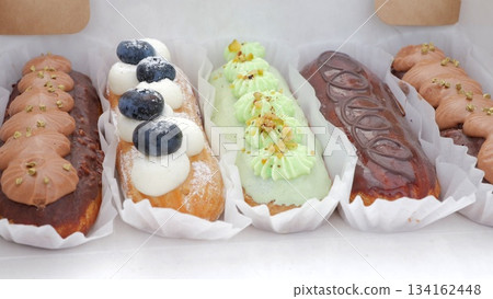 Chic eclair assortment on pristine display, Stylish pastry arrangement with sleek bakery branding elements, Sophisticated collection of confections arranged neatly for upscale cafe presentation 134162448