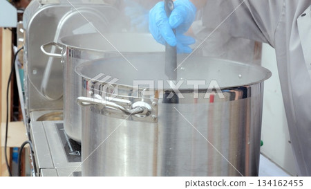 Kitchen worker prepares large volume broth, Catering staff actively cook substantial amount of savory broth, Largescale catering team diligently prepares hearty broth in busy kitchen environment Kitchen worker prepares large volume broth, Catering staff actively cook substantial amount of savory broth, Largescale catering team diligently prepares hearty broth in busy kitchen environment 134162455