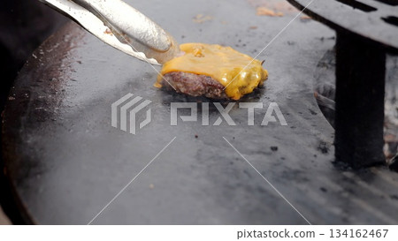 Hot burger grilling, Flavorful beef patty cooking on sizzling griddle with melting cheese and smoky scent, Vibrant outdoor food event featuring hot hamburger patty searing with melted cheese 134162467