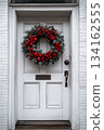 Christmas wreath with red ribbon and pine cones hangs on white door 134162555