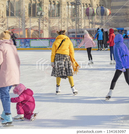 City skating rink. Crowd of people skating on festive outdoor ice rink during winter holiday in city center. Concept of seasonal celebration, urban joy, family fun 134163097