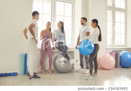 Group of young sporty people talking with coach, fitness club sportswomen holding group discussion  134163491