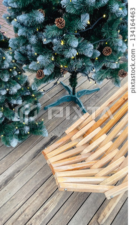 Overhead view of a decorated snowy artificial Christmas tree with pinecones next to a wooden slatted bench 134164463