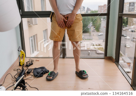 Close-up cropped shot of unrecognizable man experiencing urinary incontinence, clutching soiled shorts, highlighting distress and embarrassment associated with bladder control issues, closeup 134164516