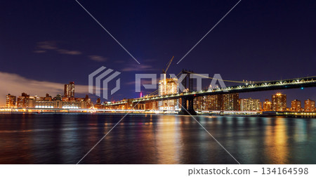 View of Manhattan Bridge New York city skyline at night with lights reflecting on water View of Manhattan Bridge New York city skyline at night with lights reflecting on water 134164598