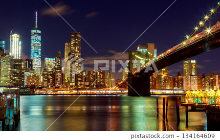 Night of Brooklyn Bridge, New York City skyline with lights shining brightly over water 134164609