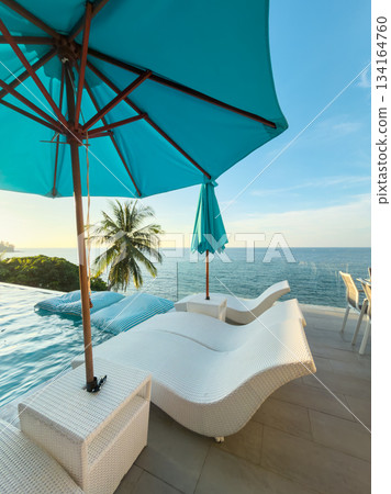 View from luxury villa at sunset, sun loungers for sunbathing, umbrellas from the sun, pillows for swimming in the pool, palm tree on background View from luxury villa at sunset, sun loungers for sunbathing, umbrellas from the sun, pillows for swimming in the pool, palm tree on background 134164760