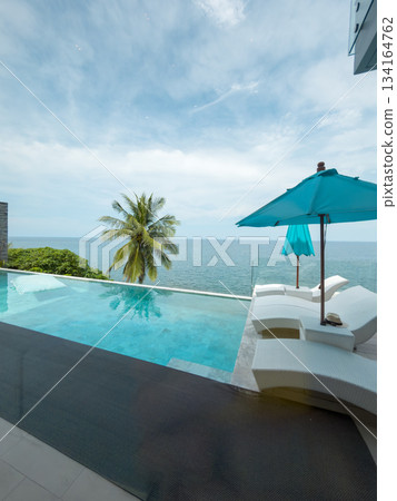 View from luxury villa at sunny day, sun loungers for sunbathing, umbrellas from the sun, pillows for swimming in the pool, palm tree on background View from luxury villa at sunny day, sun loungers for sunbathing, umbrellas from the sun, pillows for swimming in the pool, palm tree on background 134164762