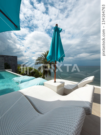 View from luxury villa at sunny day, sun loungers for sunbathing, umbrellas from the sun, pillows for swimming in the pool, palm tree on background View from luxury villa at sunny day, sun loungers for sunbathing, umbrellas from the sun, pillows for swimming in the pool, palm tree on background 134164763
