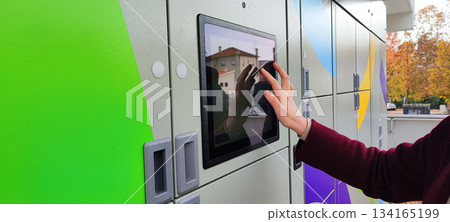 A close-up of a person's hand on the touchscreen of a street mailbox. Conceptually, it represents modern delivery services, online shopping, self-service technologies, and last-mile logistics. 134165199