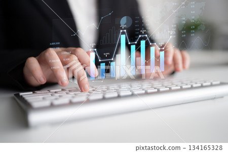 Business professional analyzing data trends with graphs and charts on a computer keyboard in a modern office setting, showcasing digital analytics for success Scalp 134165328