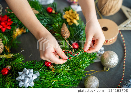 Close-up of small hands holding a decorated Christmas wreath during a holiday craft activity. A symbolic moment of festive creativity and childhood involvement in home traditions. Close-up of small hands holding a decorated Christmas wreath during a holiday craft activity. A symbolic moment of festive creativity and childhood involvement in home traditions. 134165708
