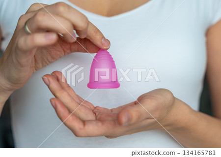 Close-up of a woman holding a pink menstrual cup in her hands, preparing for use. Promoting sustainable hygiene, personal care, and eco-friendly period products. Close-up of a woman holding a pink menstrual cup in her hands, preparing for use. Promoting sustainable hygiene, personal care, and eco-friendly period products. 134165781