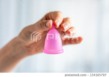 Close-up of a pink menstrual cup standing upright on a woman open palm over wooden table. Feminine hygiene product promoting zero waste, comfort, and sustainable period care. Close-up of a pink menstrual cup standing upright on a woman open palm over wooden table. Feminine hygiene product promoting zero waste, comfort, and sustainable period care. 134165797