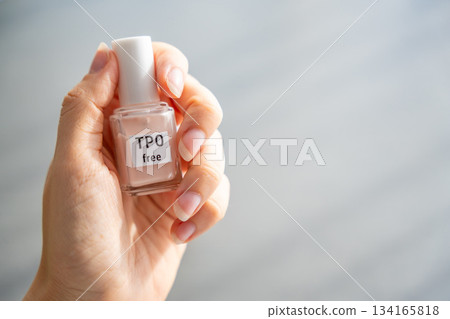 Woman holding a bottle of TPO free gel polish in bright natural light. Safe manicure product without Trimethylbenzoyl Diphenylphosphine Oxide for health-conscious consumers. 134165818