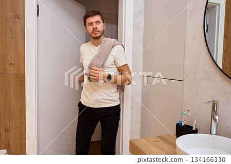 Man standing in bathroom holding towel on shoulder and opening door after hygiene routine 134166330