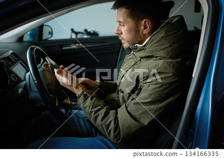 Man sitting in driver seat of car and looking at smartphone inside vehicle Man sitting in driver seat of car and looking at smartphone inside vehicle 134166335