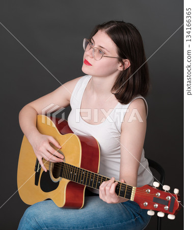 Confident female guitarist with chill expression on face, happily strumming away on classical six string acoustic guitar, totally focused on music during practice session. Guitar player from zoomers Confident female guitarist with chill expression on face, happily strumming away on classical six string acoustic guitar, totally focused on music during practice session. Guitar player from zoomers 134166365