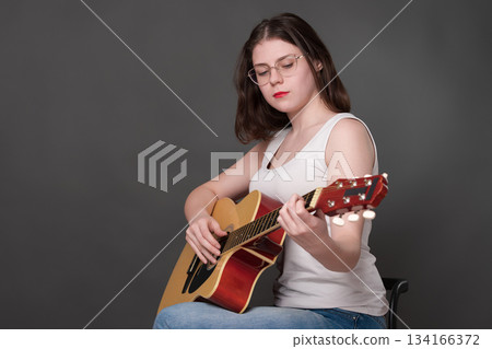 Female guitarist performing piece of music on classical guitar. Musician wearing glasses focusing intently on strings. Young adult European woman musician plays six string guitar. She member of Gen Z Female guitarist performing piece of music on classical guitar. Musician wearing glasses focusing intently on strings. Young adult European woman musician plays six string guitar. She member of Gen Z 134166372