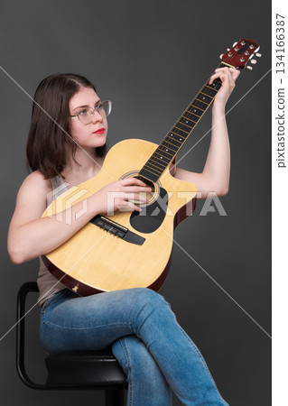Young adult female guitar player wearing glasses strumming virtuoso classical six steel string acoustic guitar fingerstyle. Woman guitarist of Caucasian, from Generation Z, dressed in tank top, jeans Young adult female guitar player wearing glasses strumming virtuoso classical six steel string acoustic guitar fingerstyle. Woman guitarist of Caucasian, from Generation Z, dressed in tank top, jeans 134166387