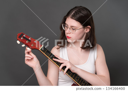 Young woman guitarist holding guitar and tuning strings of musical instrument, tightening and loosening strings before beginning to play six string acoustic classical guitar. Selective focus 134166400
