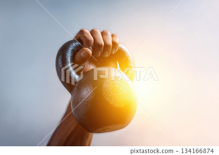 Hand lifting kettlebell against soft bright background, showing strength, fitness, motivation, and determination in gym or home workout setting 134166874