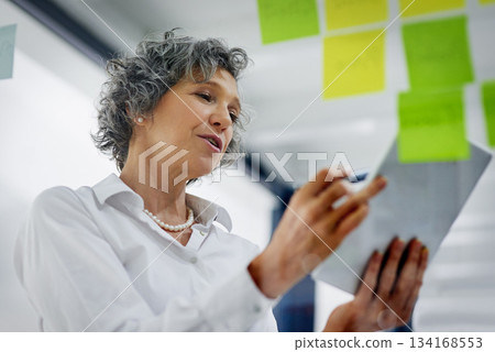 Glass wall, tablet and business woman planning, strategy and research in workplace. Sticky notes, brainstorming and senior female professional with technology for working, schedule and low angle. 134168553