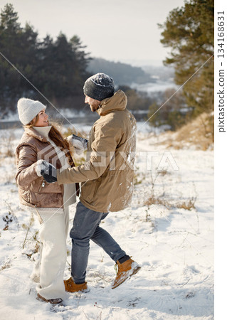 Portrait of romantic couple having fun on winter walk. Man and woman holding hands. Family wearing warm jacket and knitted hats. 134168631